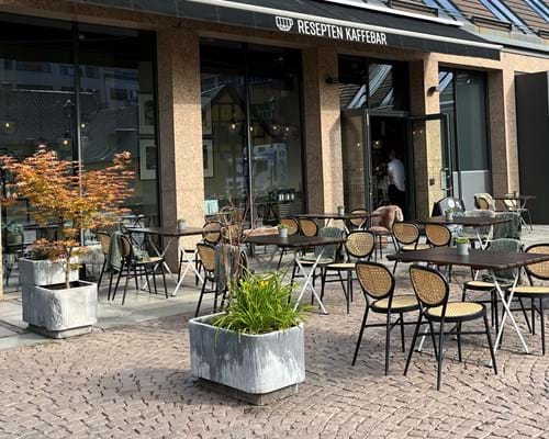 Uteserveringen på Resepten Kaffebar består av firkantede bord i treverk og stoler i lys rotting.